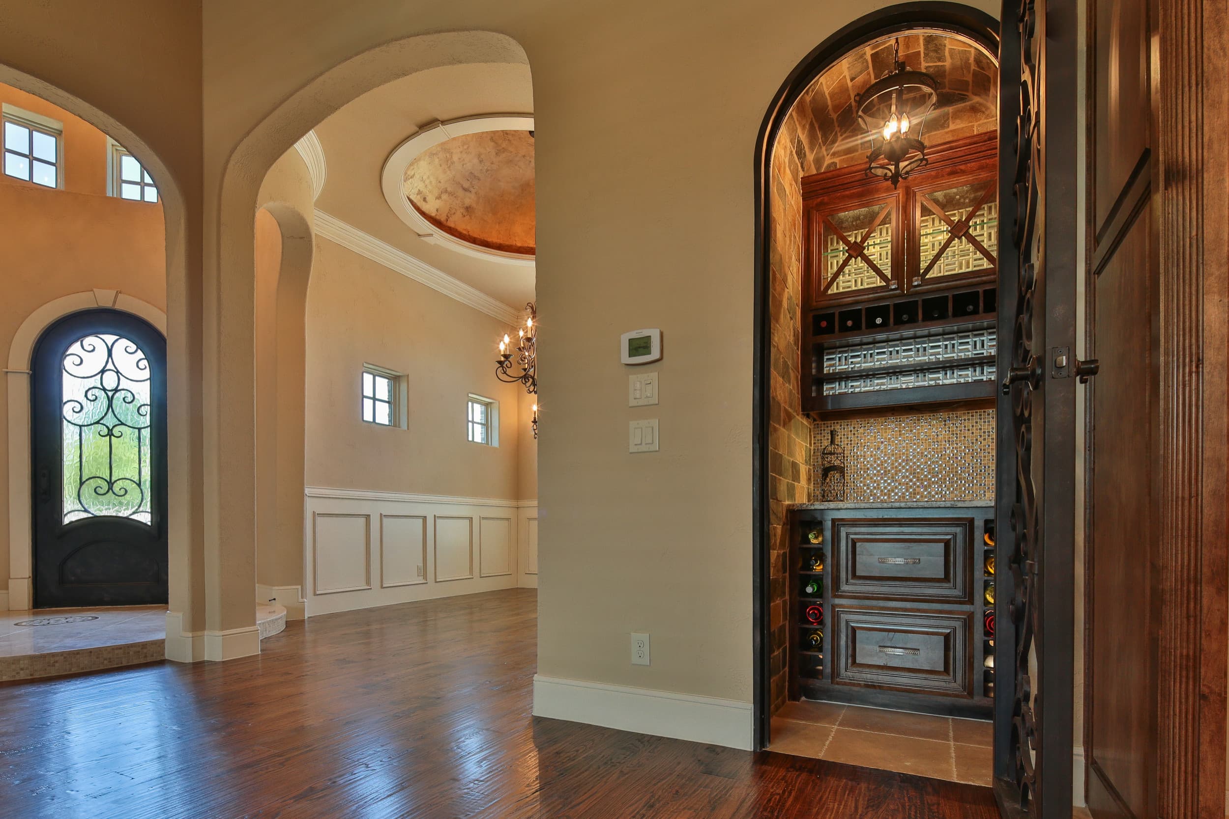 Arched wine closet with wrought iron door, stone vaulted ceiling, lantern pendant, mosaic tile backsplash, and stained cabinetry with wine cubbies