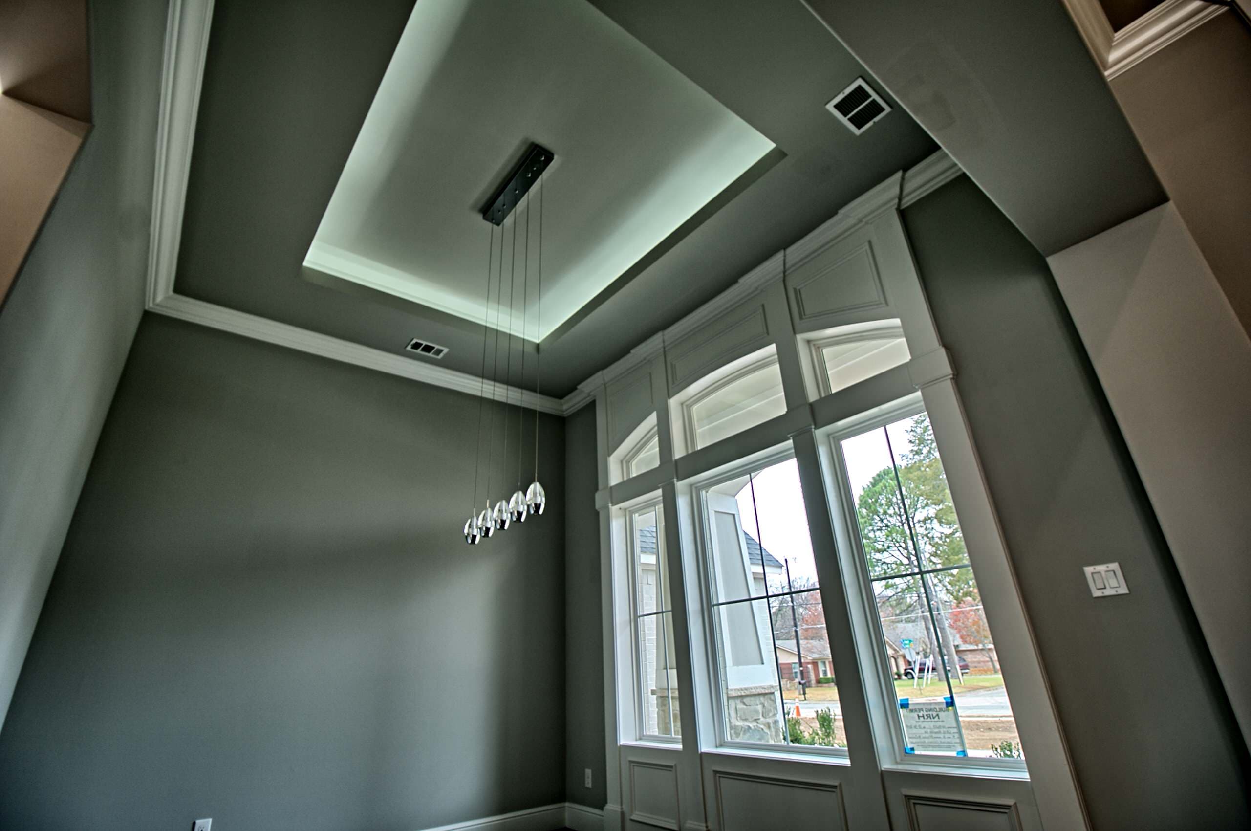 Tall room with a tray ceiling and cove lighting, a linear five-light glass pendant and arched-transom windows framed in white paneled millwork