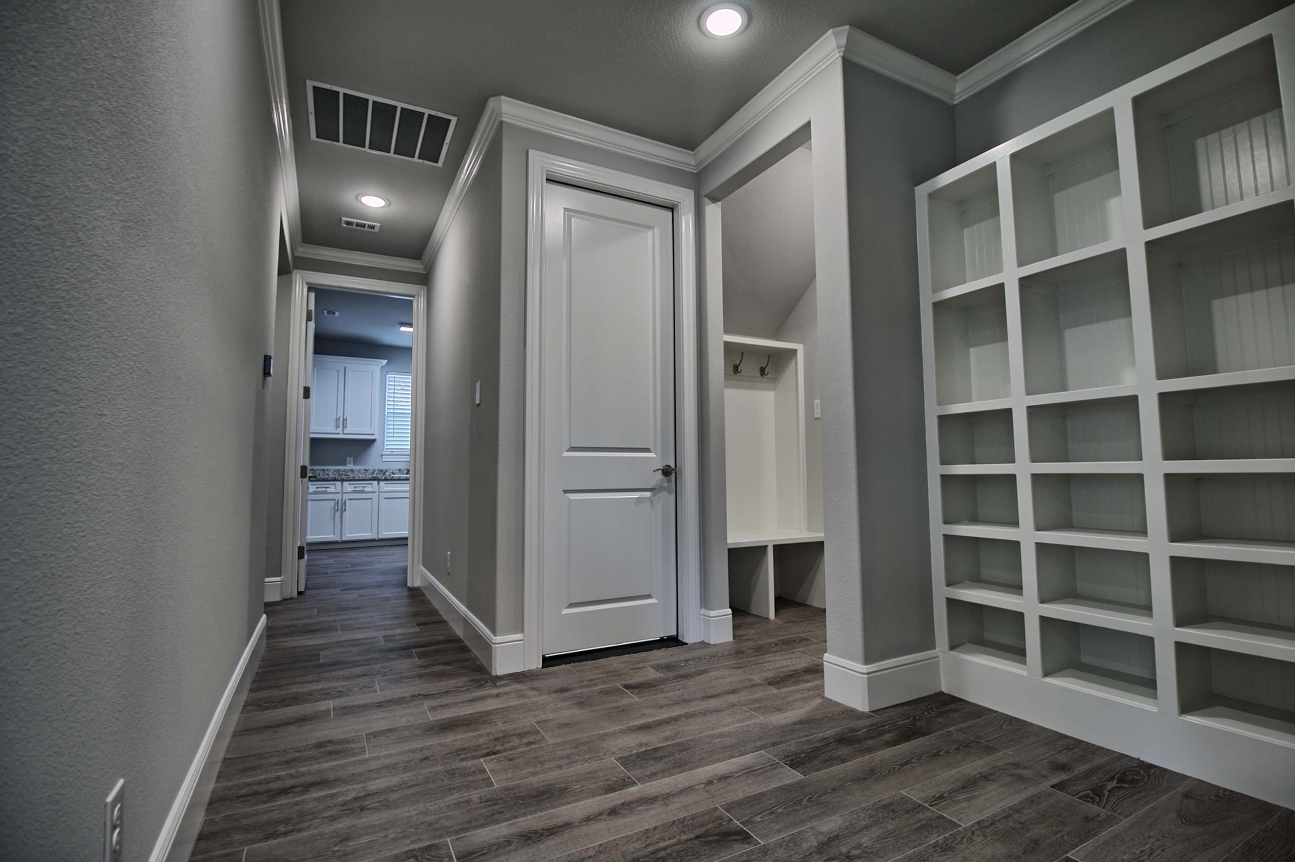 Hall with built-in white cubbies, bench nook with coat hooks and wood-look tile floor, leading to a laundry room with white cabinets
