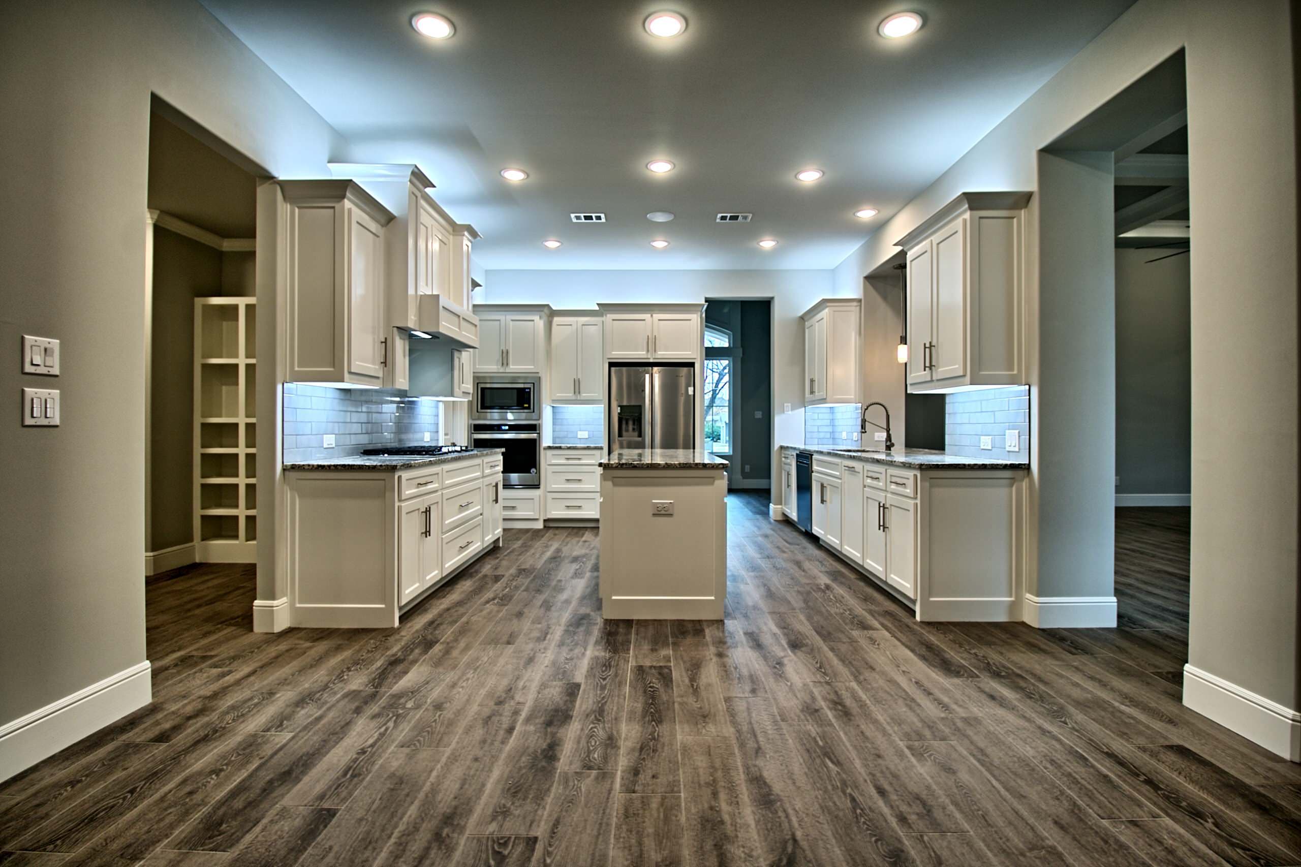 White shaker kitchen with center island, granite counters, gray subway tile and stainless appliances, flanked by wide openings to adjoining rooms
