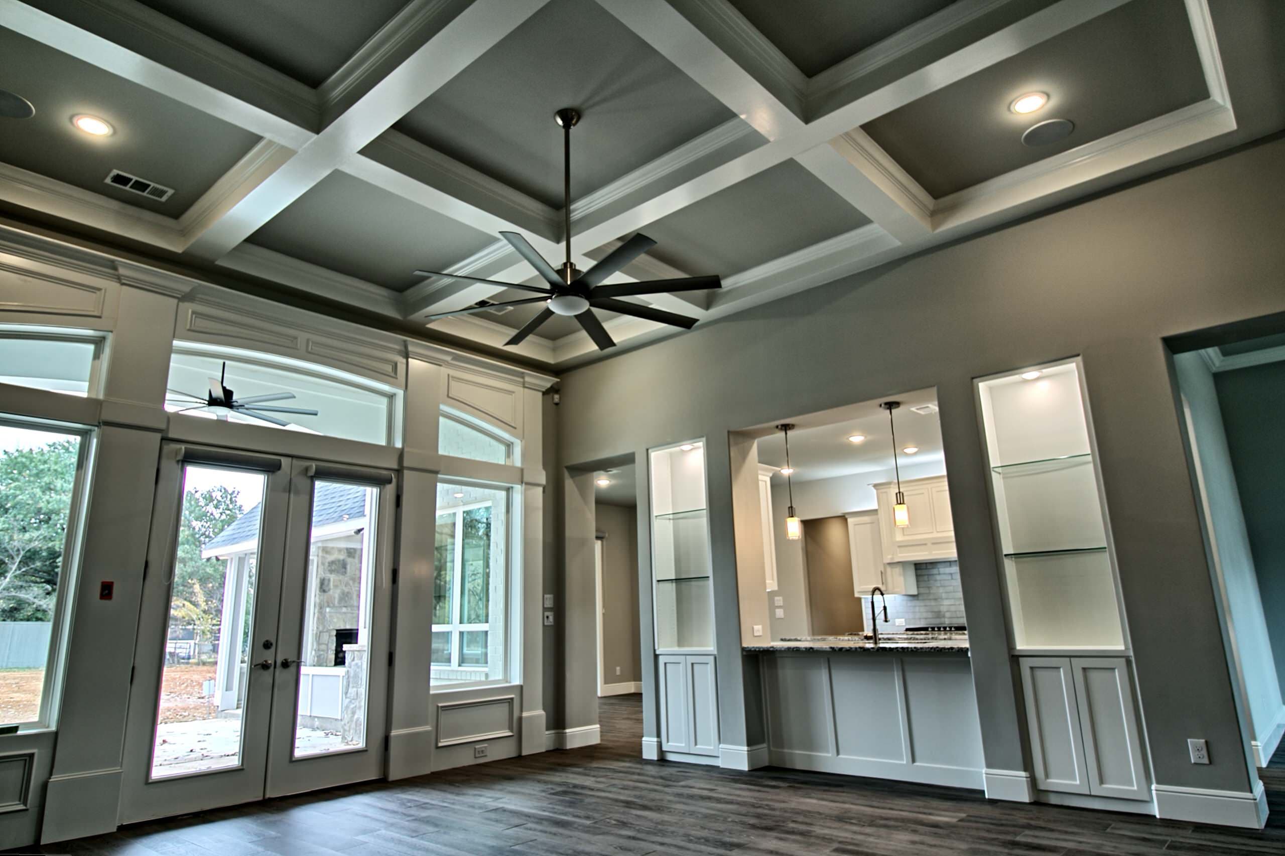 Living room with coffered ceiling, eight-blade fan, French doors to a covered patio and a kitchen pass-through between lit display niches