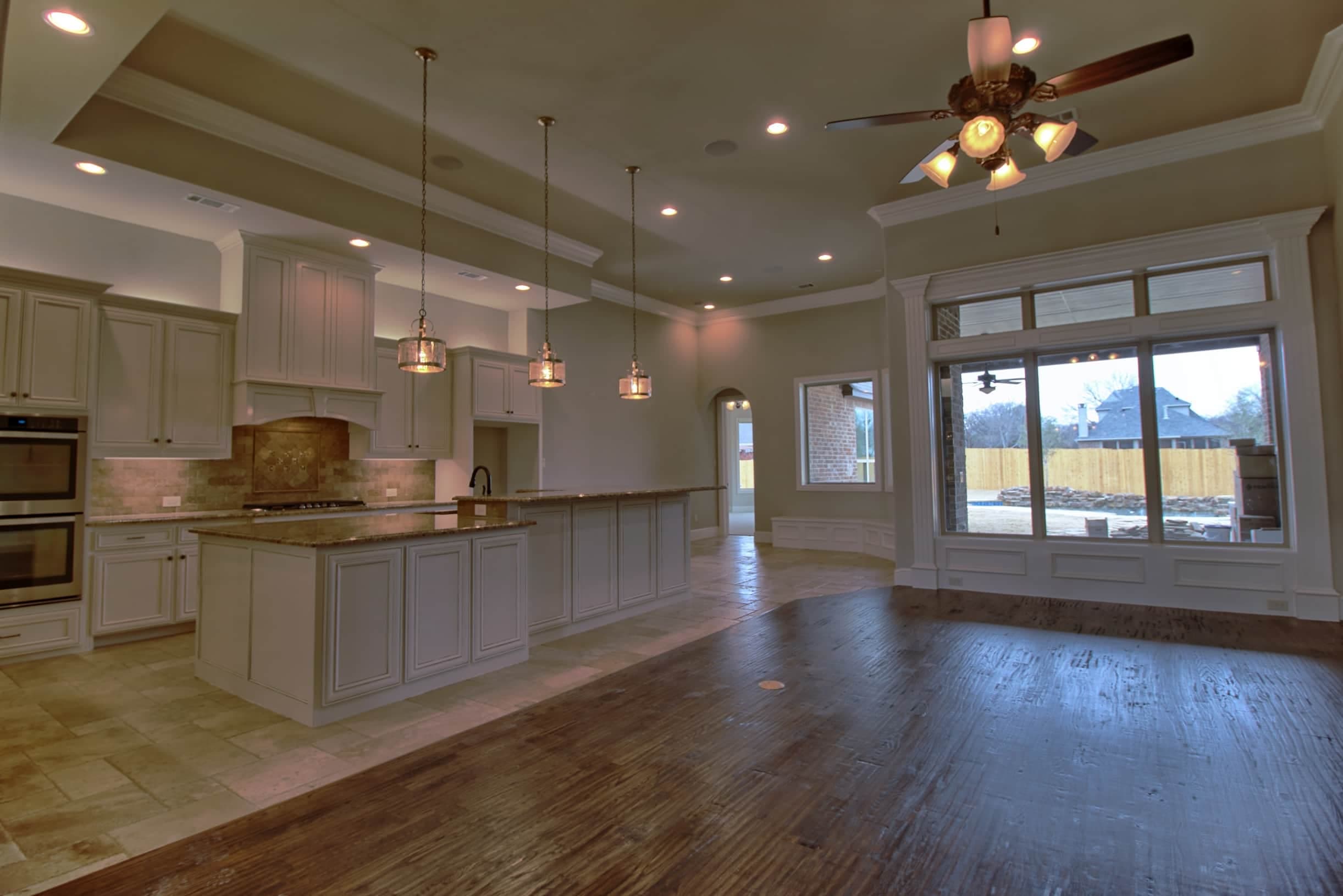 Luxury custom kitchen and living space by Oakmark Custom Homes featuring large island, pendant lighting, and open-concept design with oversized windows.