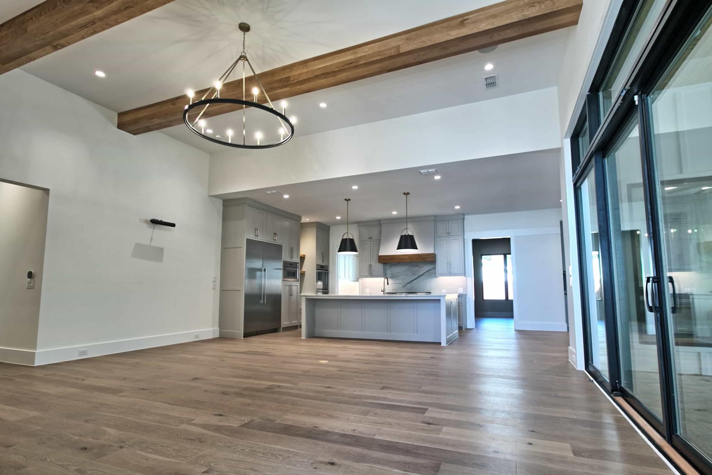 Luxury open-concept kitchen and living room built by Oakmark Custom Homes, featuring custom cabinetry, wood beams, and wide-plank oak flooring.