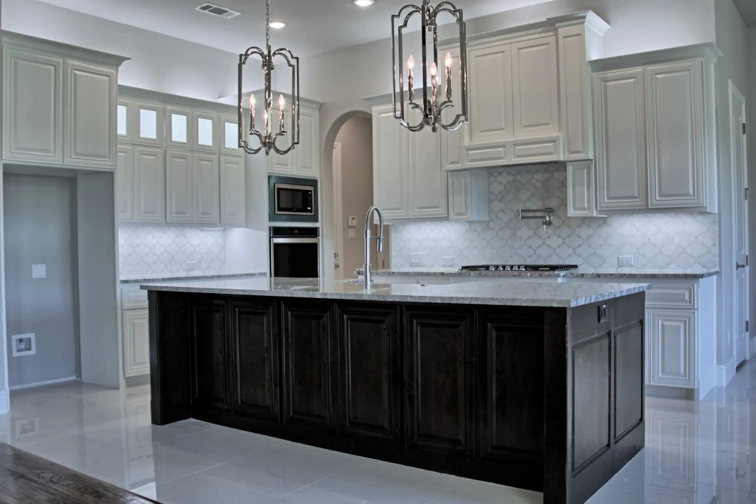 Modern luxury kitchen with white upper cabinets, dark wood island, stainless steel appliances, marble countertops, and pendant lighting.