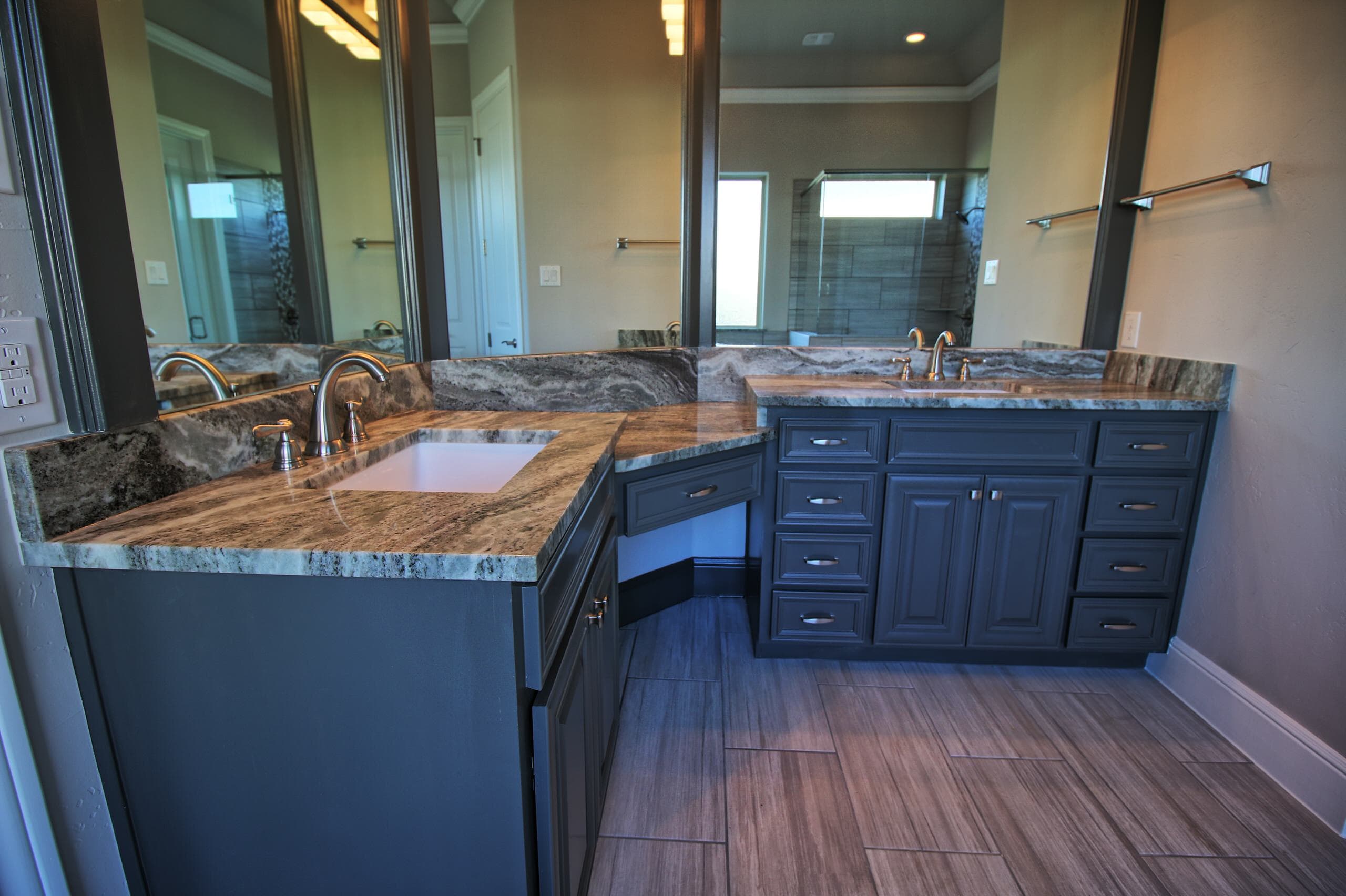 Angled double vanity with charcoal cabinets, swirled gray stone counters, undermount sinks, brushed nickel faucets, and a knee-space section between