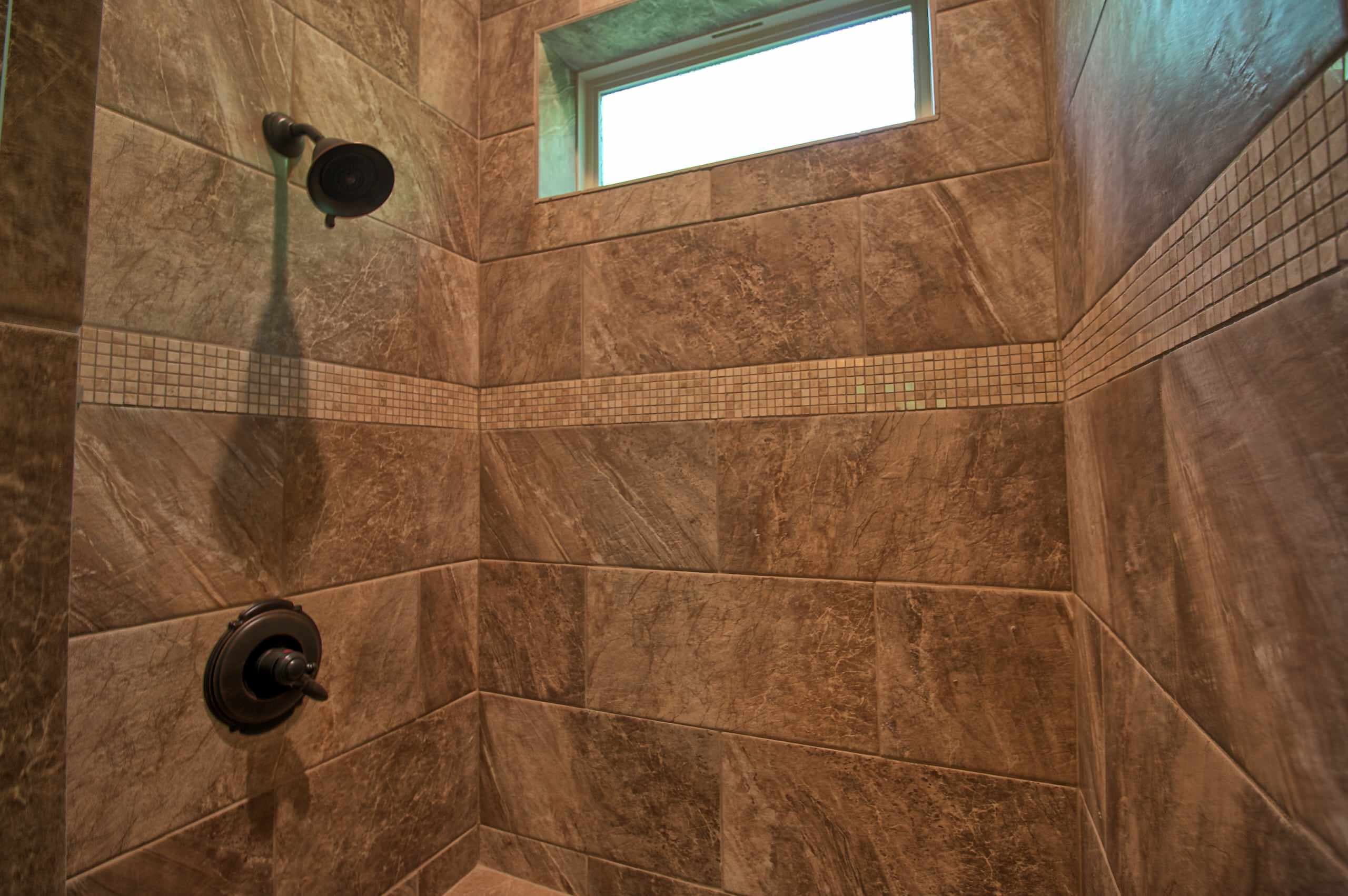 Shower with large brown marble-look wall tile, a cream mosaic band, oil-rubbed bronze showerhead and valve trim, and a high window