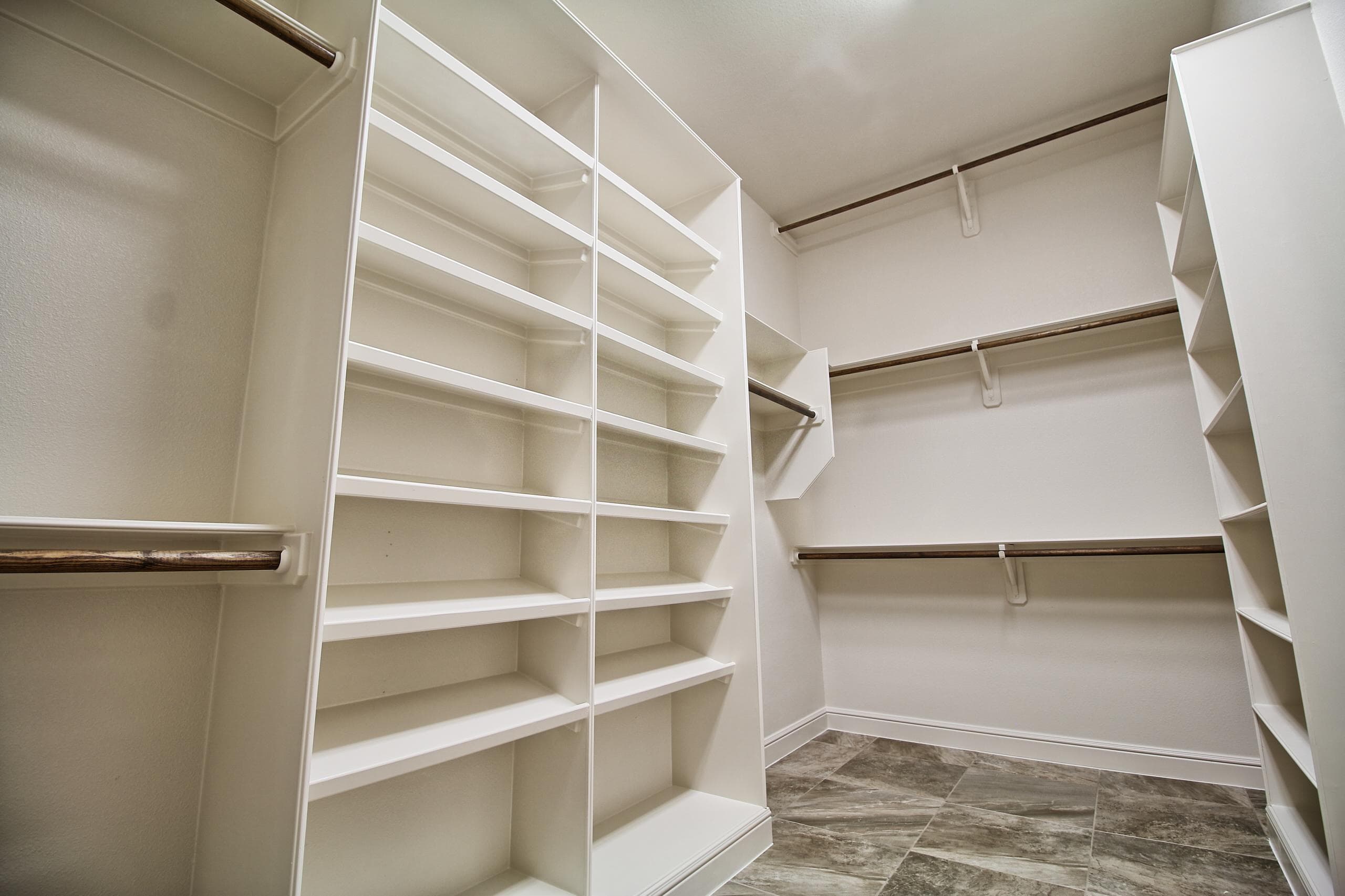 Walk-in closet with white built-in shelving towers, double-hang stained wood rods and diagonal marble-look tile floor