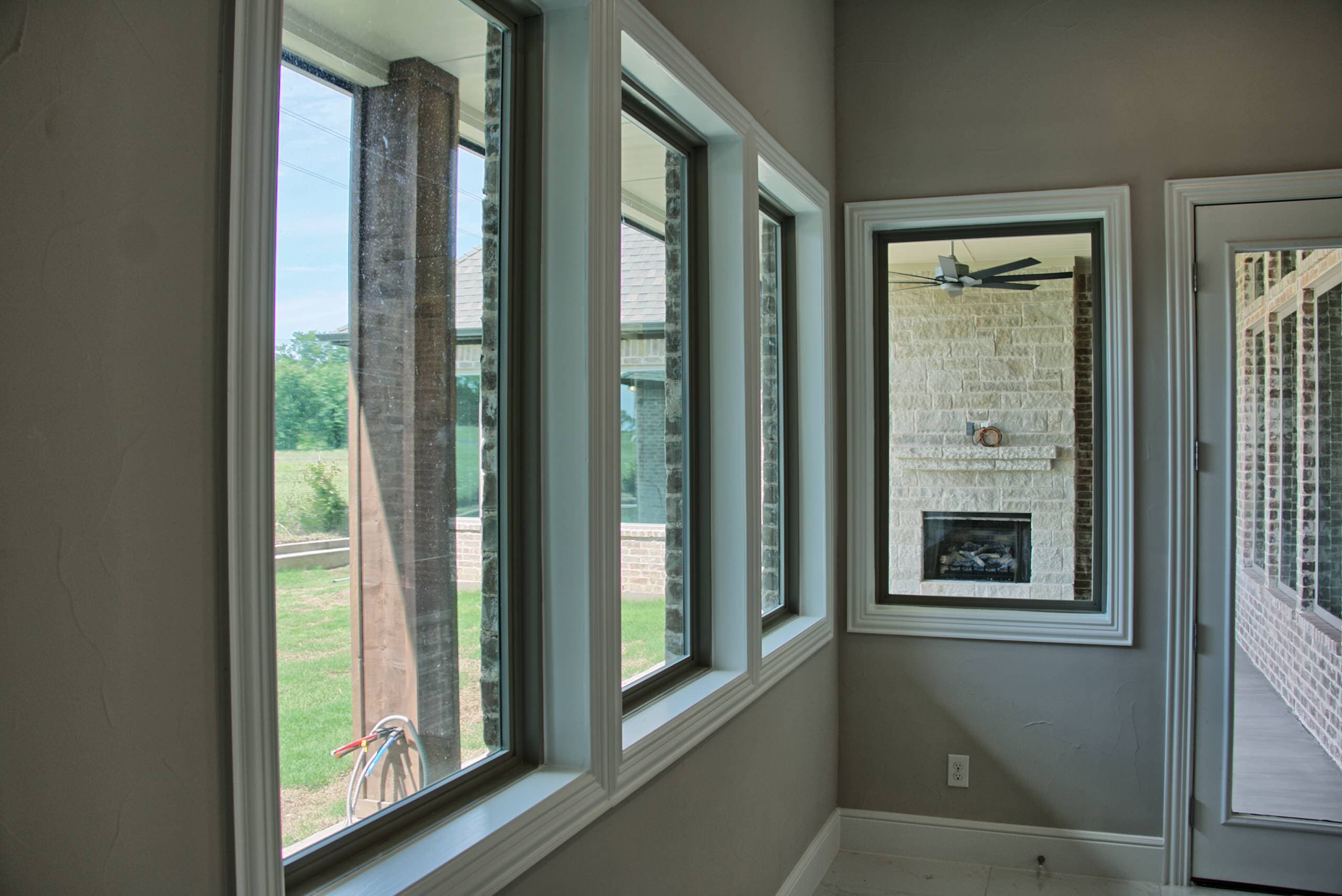 Room corner with tall dark-framed windows and a glass door overlooking a covered patio with stone outdoor fireplace and ceiling fan