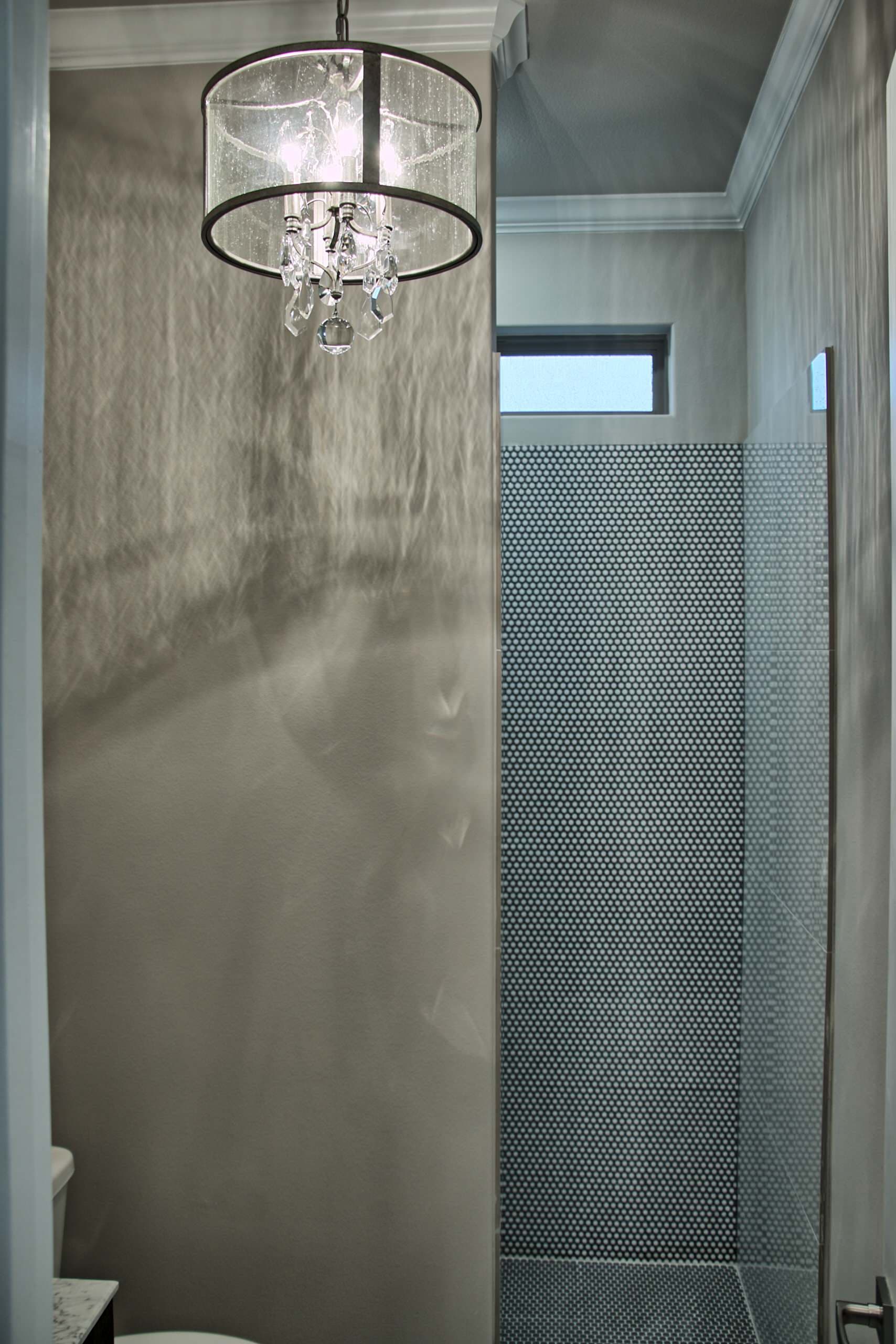 Seeded glass drum chandelier with crystal drops, gray walls, crown molding and a walk-in shower lined in charcoal penny tile