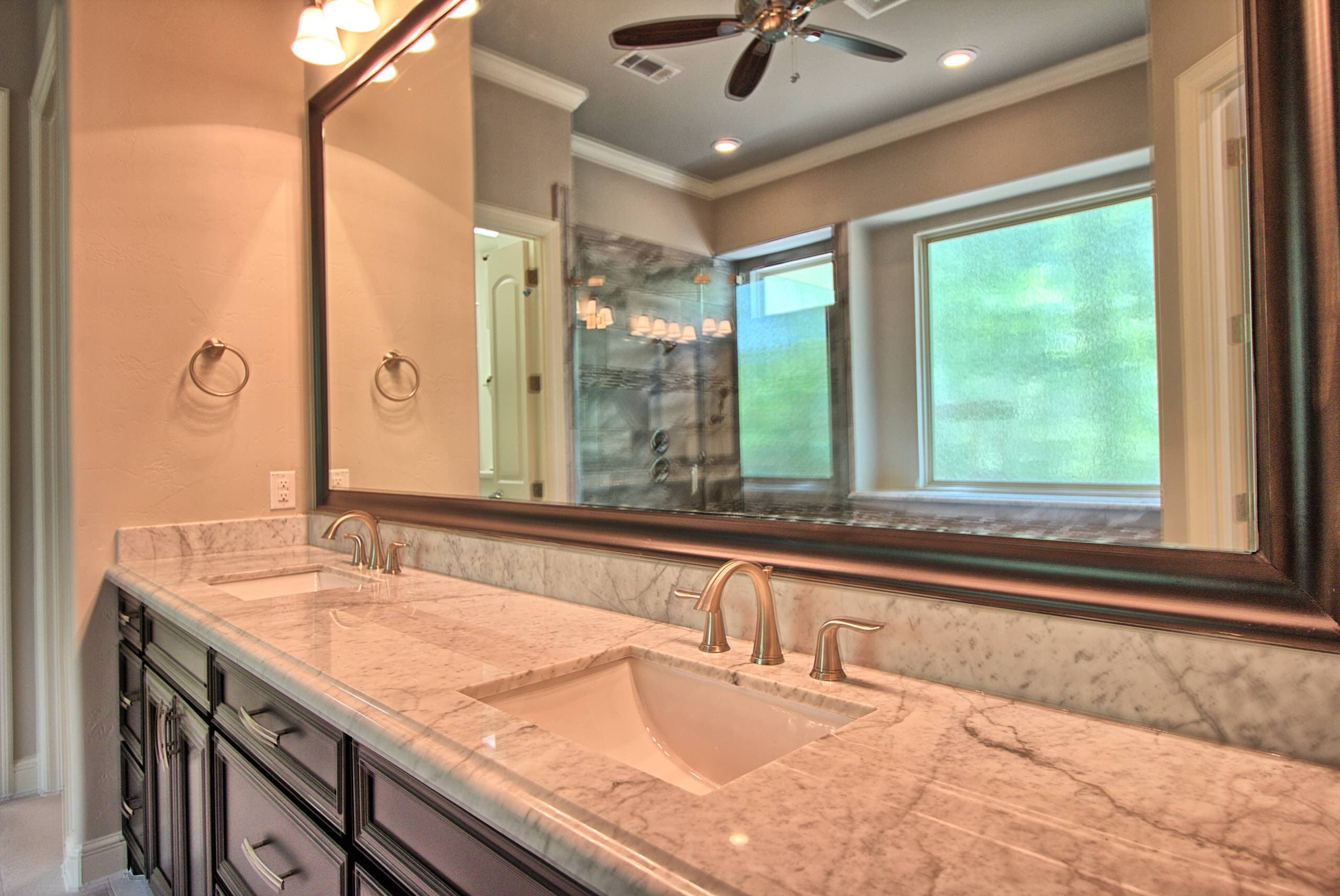 Double vanity with white marble countertop and backsplash, two undermount sinks, brushed nickel faucets, dark cabinetry and a large framed mirror