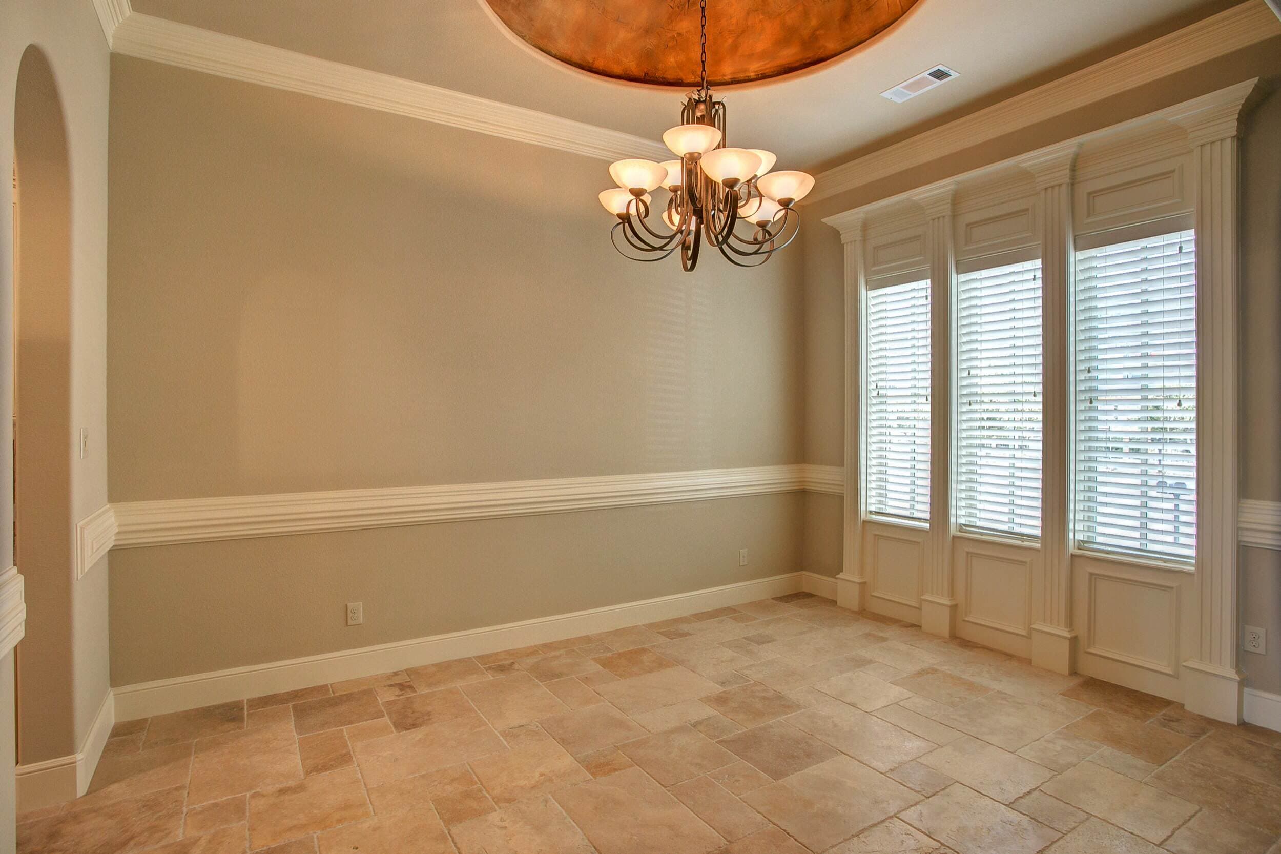 Dining room with copper faux-finished ceiling dome, bronze chandelier, chair rail, travertine floor and three tall windows framed by fluted pilasters