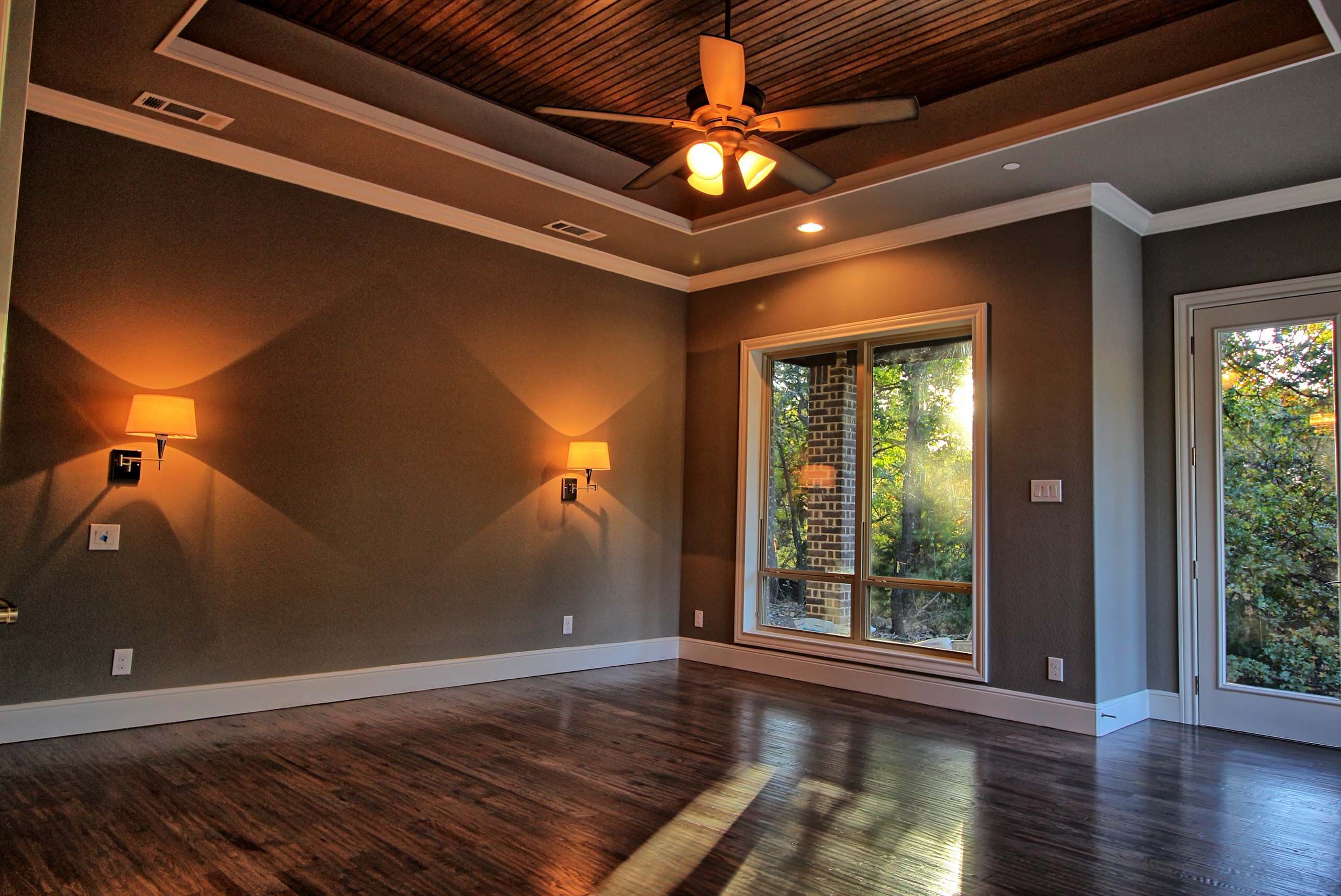 Bedroom with stained wood plank tray ceiling, ceiling fan, swing-arm wall sconces, hardwood floors, a large window and glass exterior door