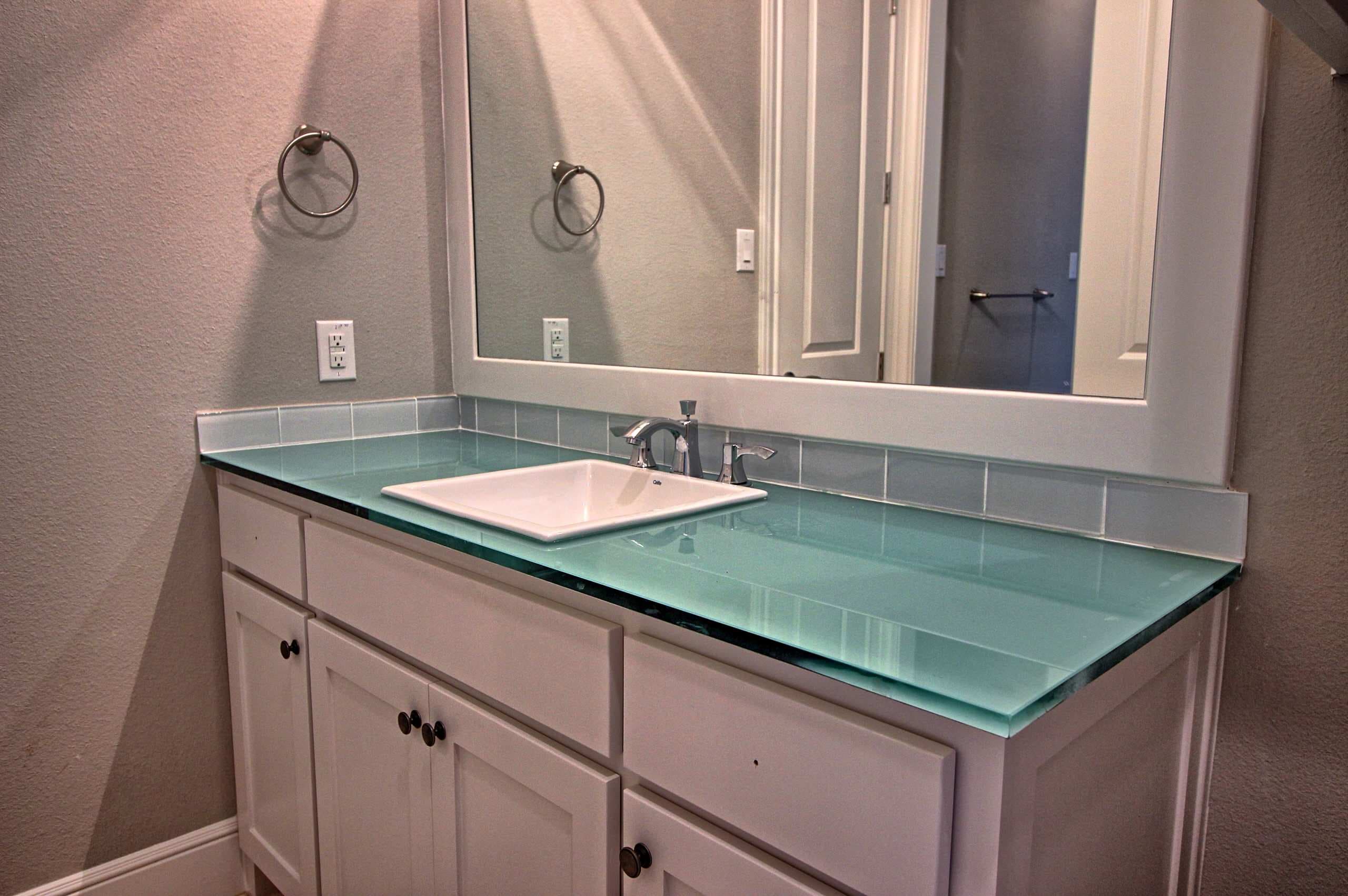 Bathroom vanity with white shaker cabinet, thick aqua glass countertop, square drop-in sink, chrome faucet, glass tile backsplash and white framed mirror