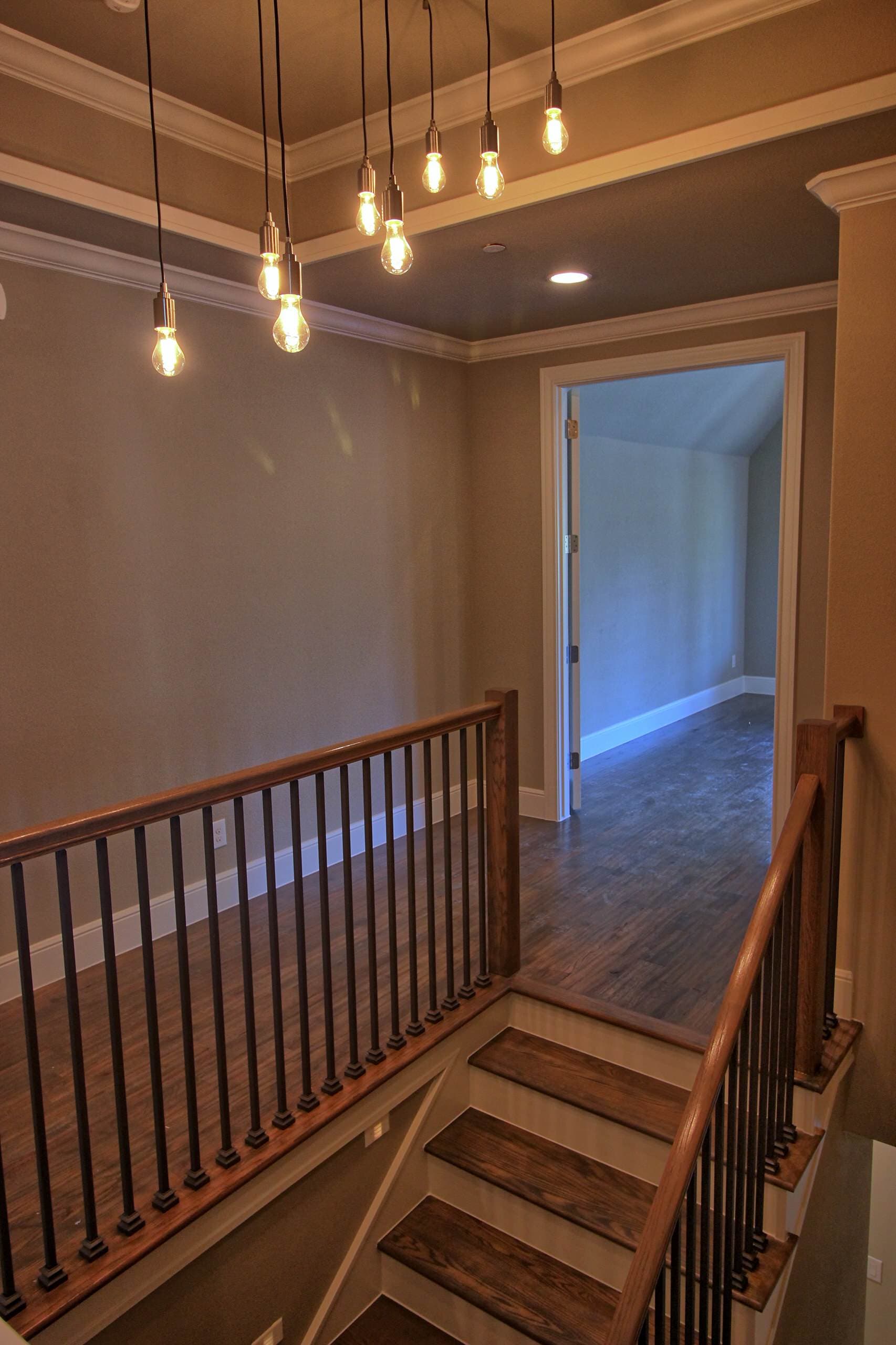 Upstairs landing with a cluster of bare-bulb pendants, stained wood handrail and treads, black iron balusters, white risers and hardwood floors