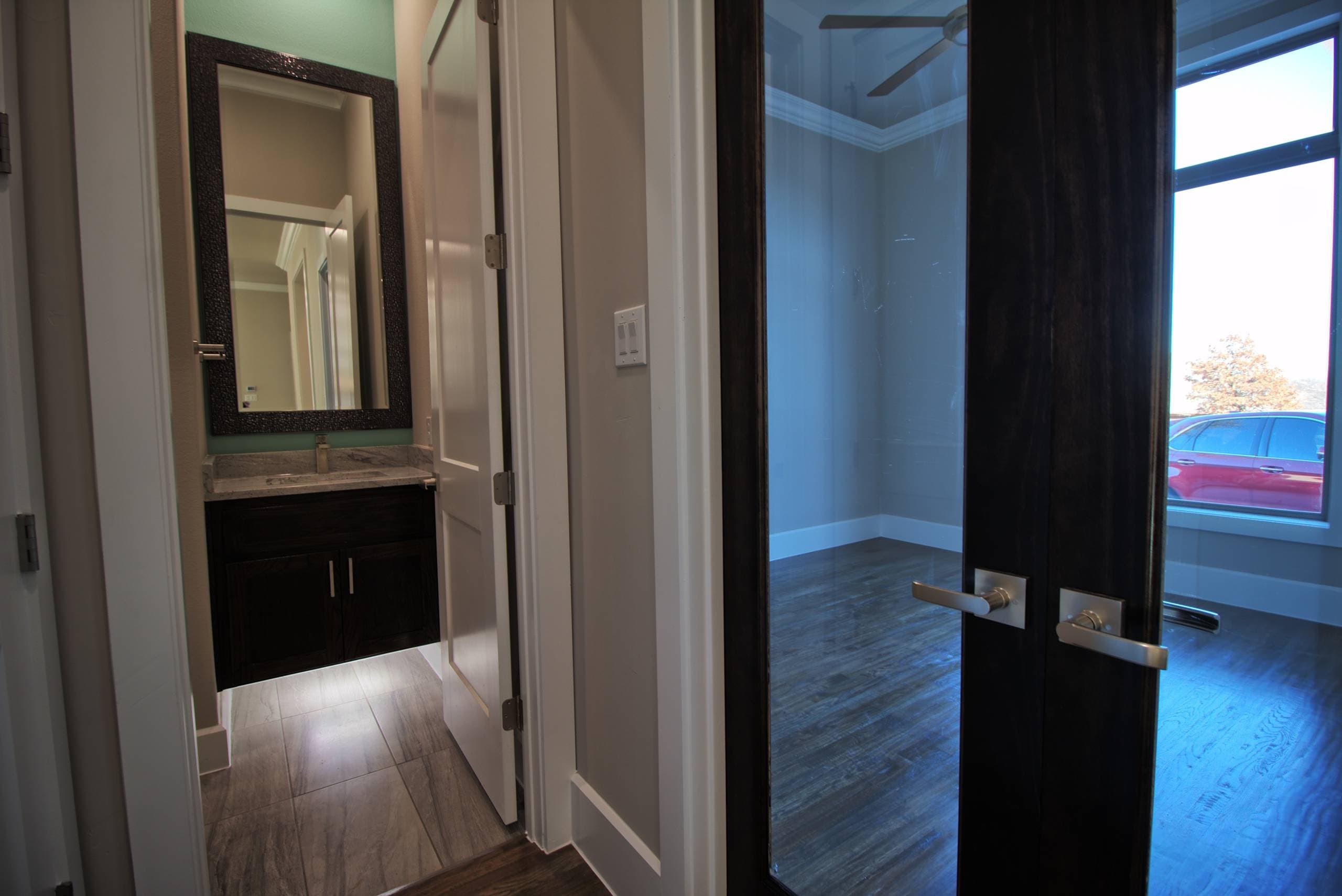 Bathroom with floating dark wood vanity, granite top, framed mirror, and aqua accent wall, beside dark glass-paneled French doors