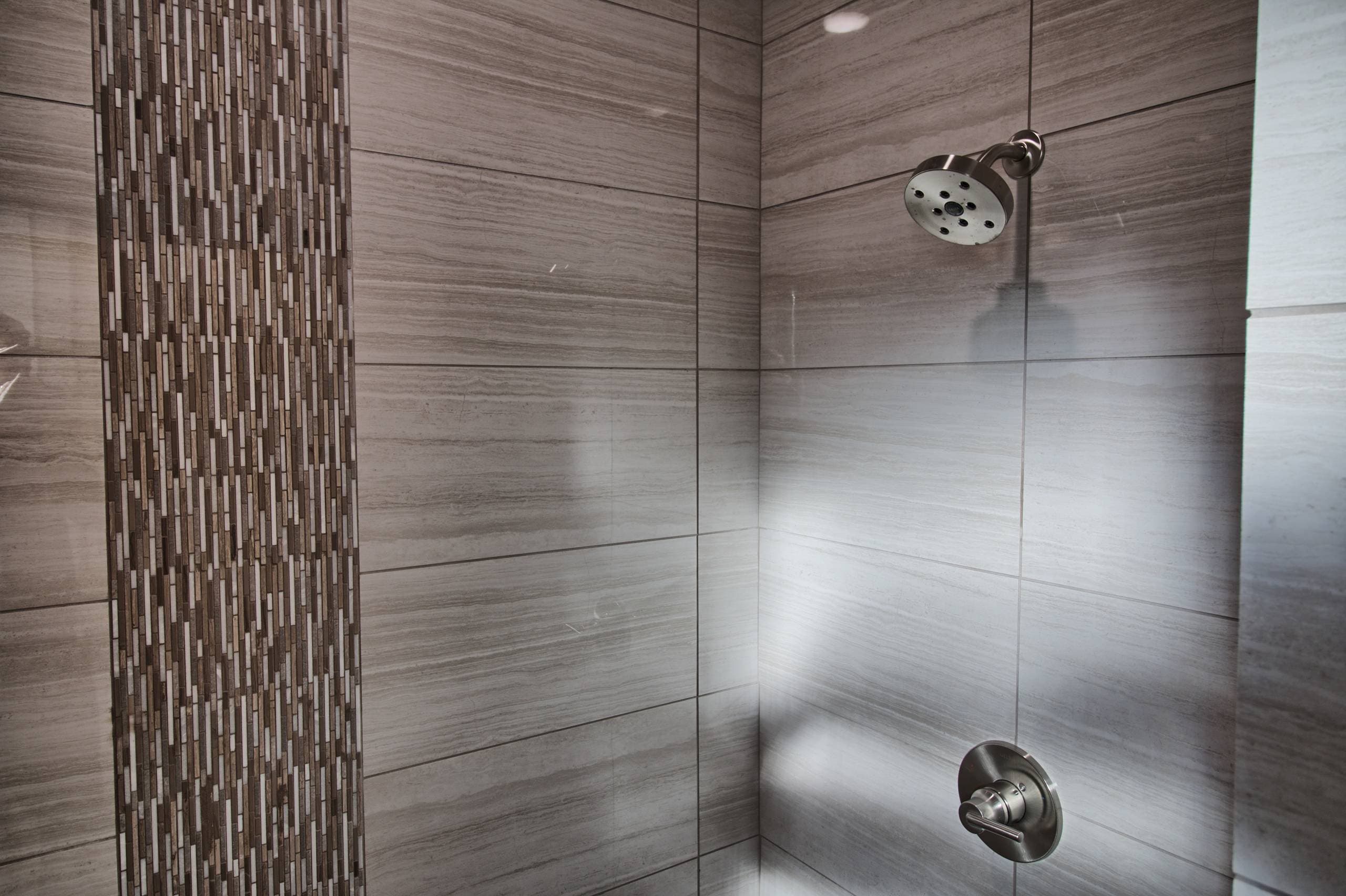 Shower with large gray linear-veined tile, a vertical mosaic accent strip, and brushed nickel round showerhead and valve trim