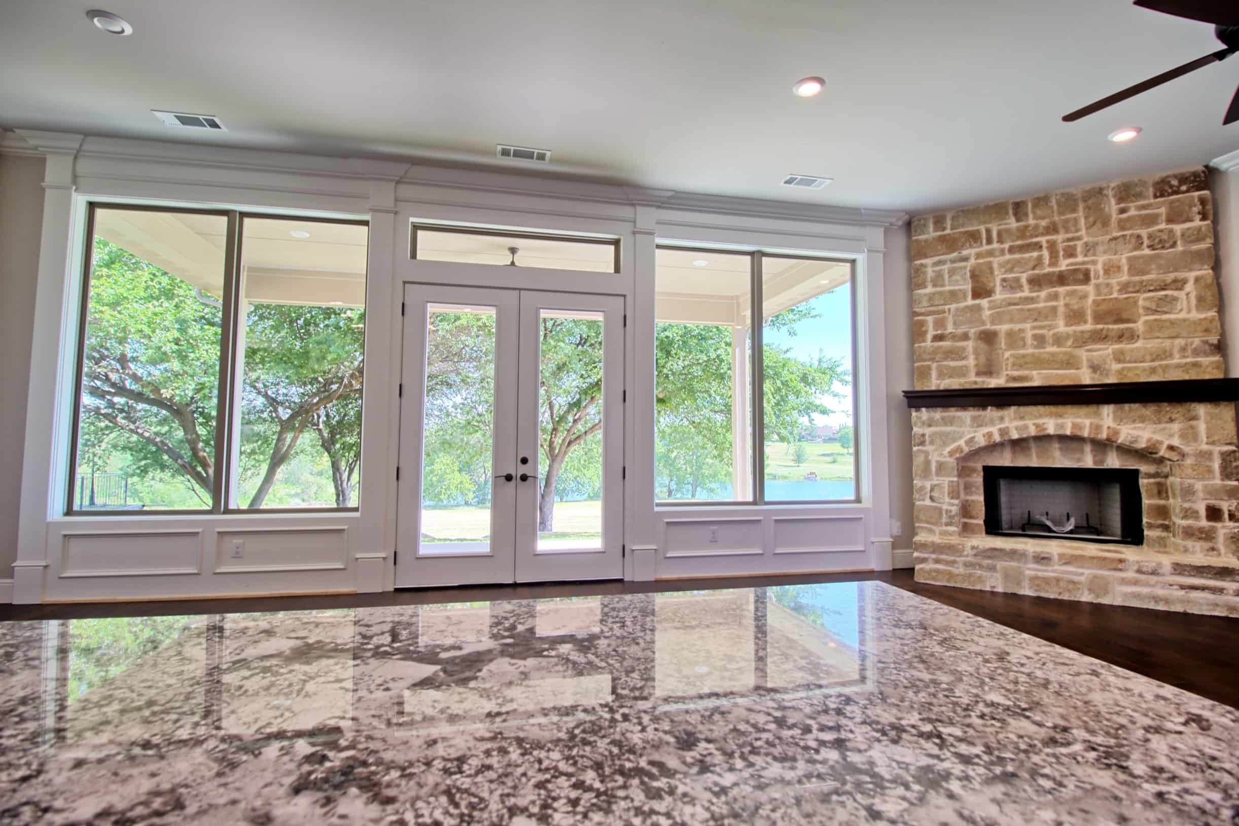 Luxury living room in an Oakmark Custom Homes custom build featuring floor-to-ceiling windows, stone fireplace, and elegant French doors overlooking scenic views.