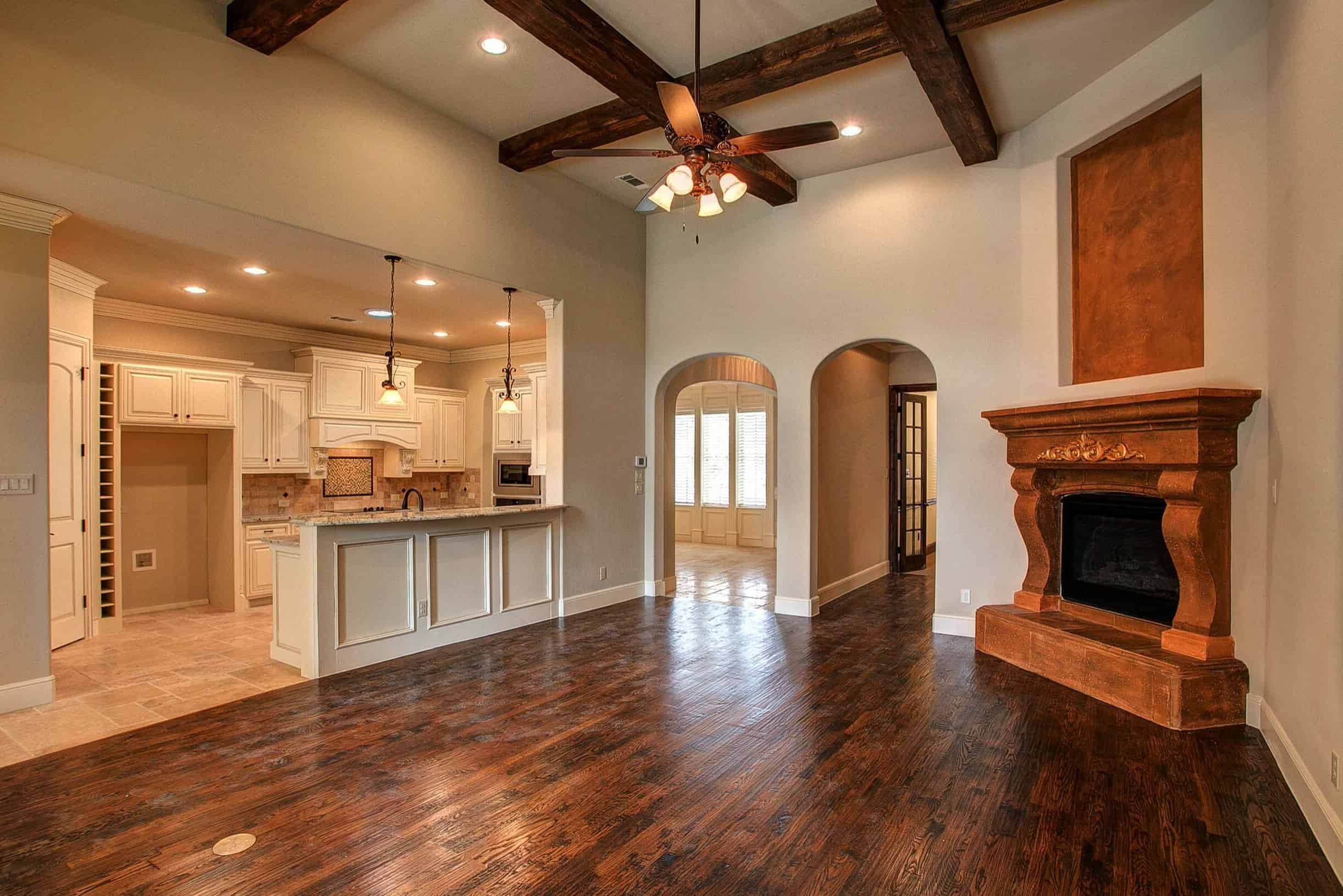 Luxury open-concept living space by Oakmark Custom Homes with rustic fireplace, wood beams, and custom kitchen with white cabinetry.