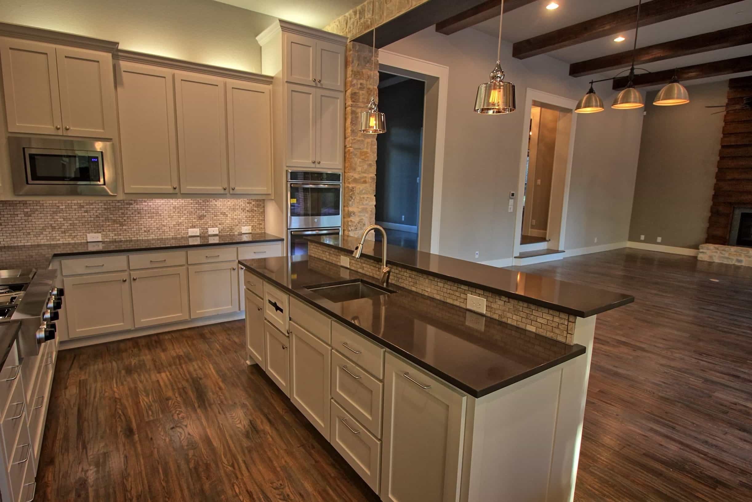 Custom kitchen by Oakmark Custom Homes featuring quartz countertops, white cabinetry, stone accents, and open-concept design with hardwood floors.