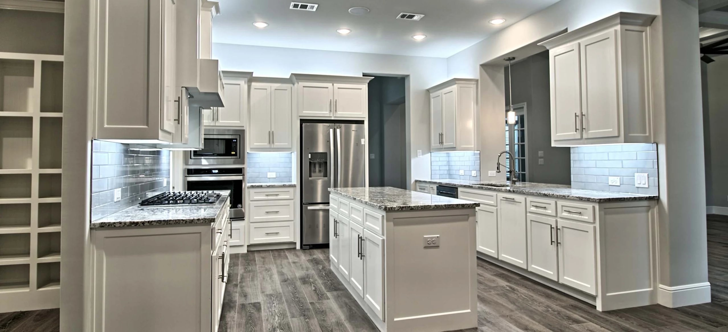 Kitchen with white shaker cabinetry, granite counters, gray subway tile backsplash, a center island and wood-look plank floors